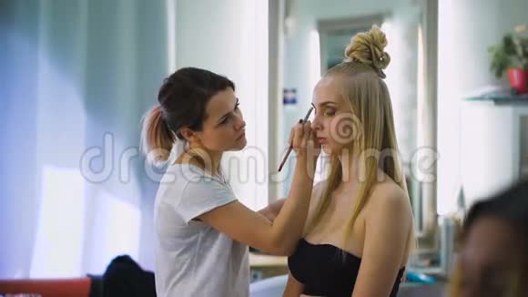 专业美容师和设计师在工作对于一个壮观的顶级模特做一个明亮富有表现力的化妆时尚视频的预览图
