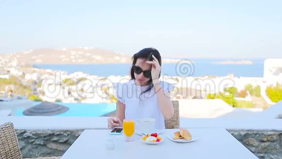 美丽优雅的女士在室外咖啡馆吃早餐在Mykonos镇有令人惊叹的景色喝热咖啡的女人视频的预览图