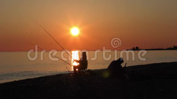 美丽的景色与渔夫剪影与鱼竿坐在海边视频的预览图