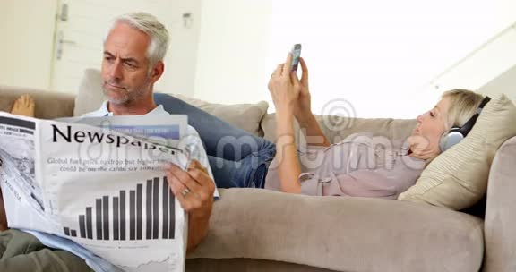 男人一边看报纸一边在沙发上听音乐视频的预览图