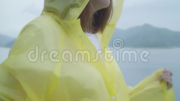 慢动作年轻的亚洲妇女感到高兴的打雨同时穿着雨衣站在湖边视频的预览图