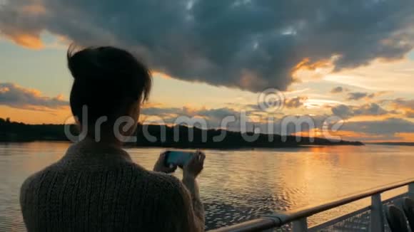 女轮廓用智能手机在游轮甲板上拍摄日落照片视频的预览图