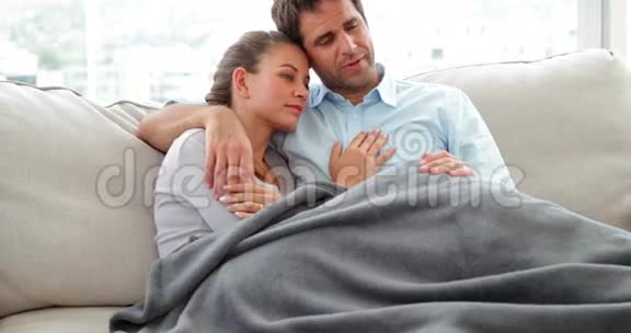 可爱的一对夫妇躺在沙发上在毯子下面聊天视频的预览图