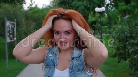年轻的红头发女人在城市公园摇头视频的预览图