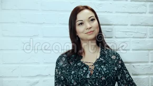 一个年轻的女人摆姿势看着白色砖墙背景上的相机视频的预览图