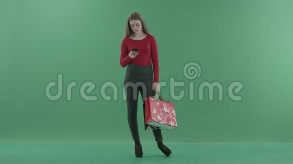 穿着便服的漂亮女人拿着购物袋在手机上发短信或上网视频的预览图