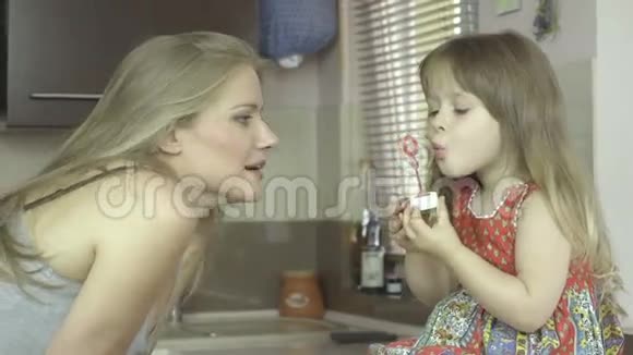 快乐的年轻母亲和女儿在厨房里吹肥皂泡视频的预览图