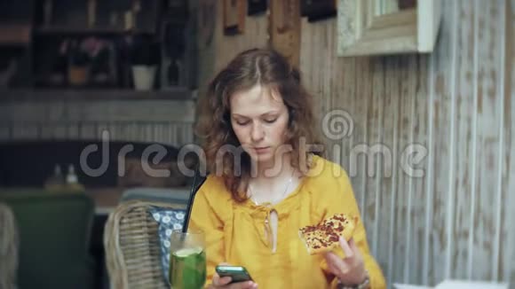 一个年轻的女人在咖啡馆里吃馅饼用电话视频的预览图