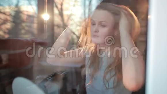 透过窗户温暖的女孩享受她的头发的肖像很漂亮的背光视频的预览图