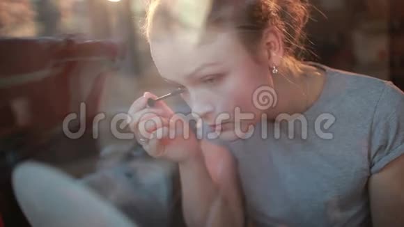 透过窗户的肖像一个漂亮的女孩在睫毛上涂睫毛膏视频的预览图