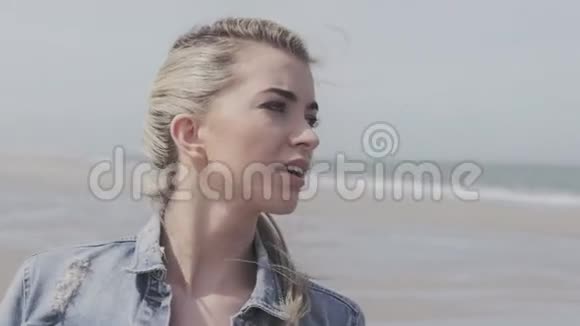 快乐的年轻女子穿着牛仔夹克在孤独的海滩上玩得开心视频的预览图