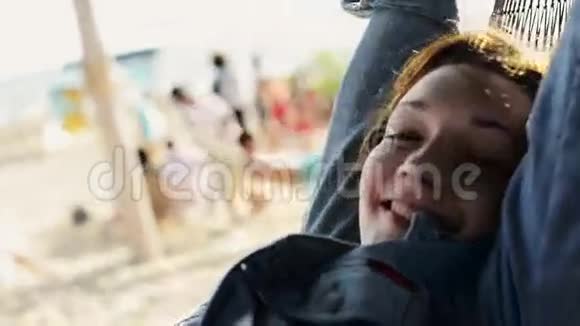 快乐的年轻女孩在沙滩上的吊床上摇摆在镜头中微笑夏日阳光明媚视频的预览图