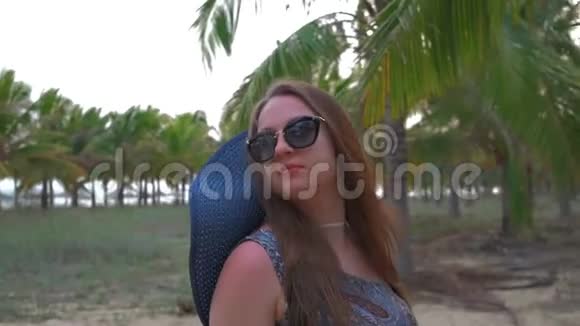 戴着蓝色帽子和眼镜的年轻女孩看着热带棕榈树近距离射击动作缓慢视频的预览图