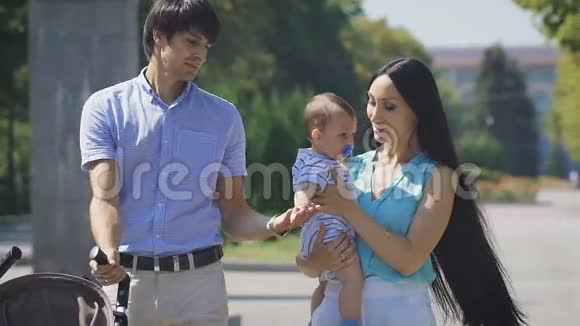 年轻的一家人抱着一个小男孩走在城市公园里视频的预览图