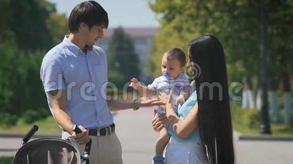 年轻的一家人抱着一个小男孩走在城市公园里视频的预览图