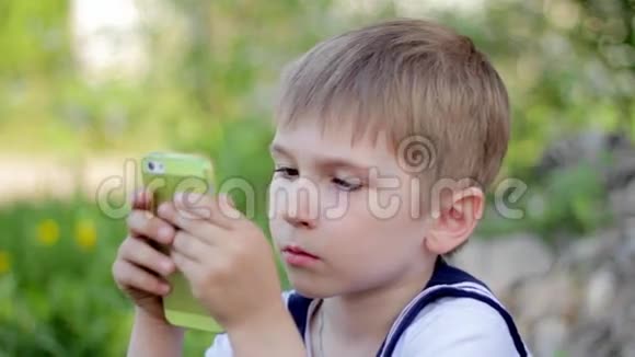 小男孩在智能手机上玩游戏春天公园视频的预览图