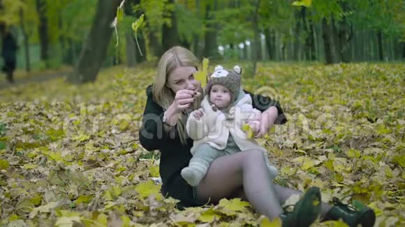 母女俩在秋天公园玩秋天父母和婴儿在森林里散步宝宝在户外玩耍视频的预览图