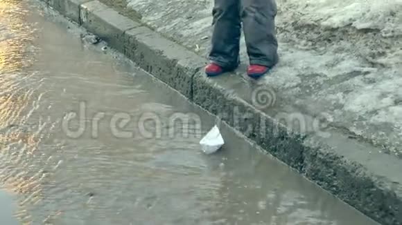 穿着橡胶靴的女孩在靠近纸船的水坑上跳跃视频的预览图