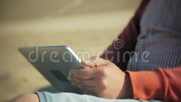 一个人坐在船边的沙滩上戴着耳机用平板电脑视频的预览图