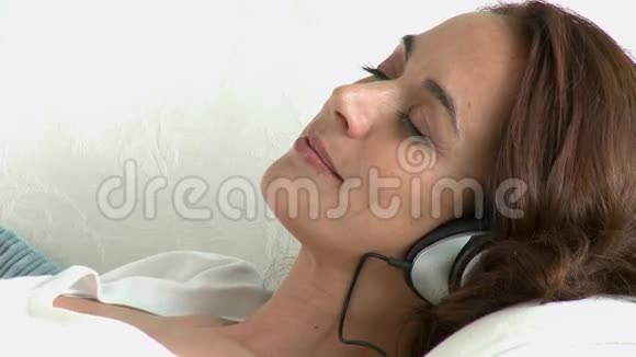 放松西班牙裔女人躺在沙发上用耳机听音乐视频的预览图
