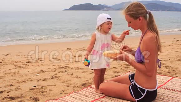 金发碧眼的母亲和小女儿坐在垫子上吃东西视频的预览图