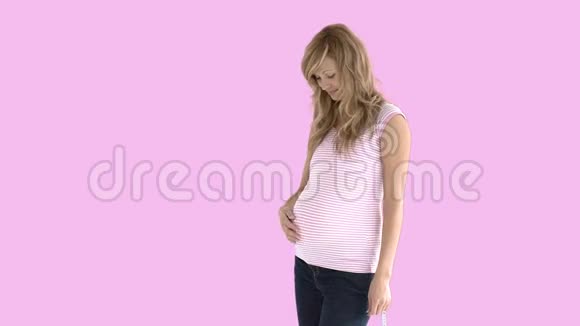 微笑的未来妈妈站在粉红色的背景下视频的预览图
