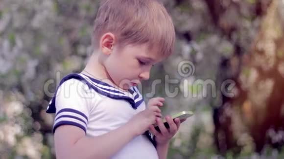 小男孩在智能手机上玩游戏春天公园视频的预览图