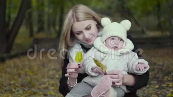 母女俩在秋天公园玩秋天父母和婴儿在森林里散步宝宝在户外玩耍视频的预览图