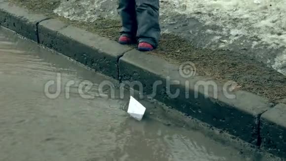 穿着橡胶靴的女孩在靠近纸船的水坑上跳跃视频的预览图