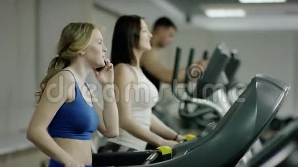 年轻微笑的金发女人在跑步机上行走视频的预览图