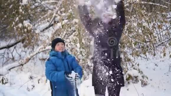 女孩和孩子把雪洒在自己身上在冬天的公园里享受它视频的预览图