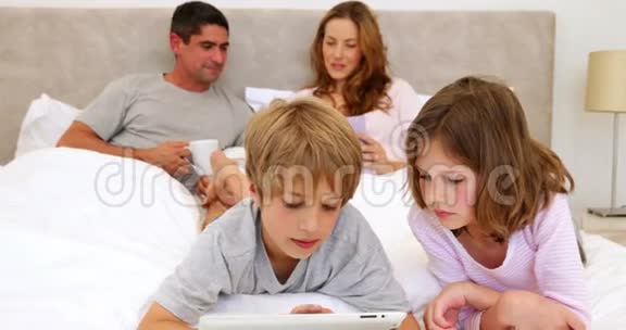 孩子们在床上用平板电脑父母在后面聊天视频的预览图