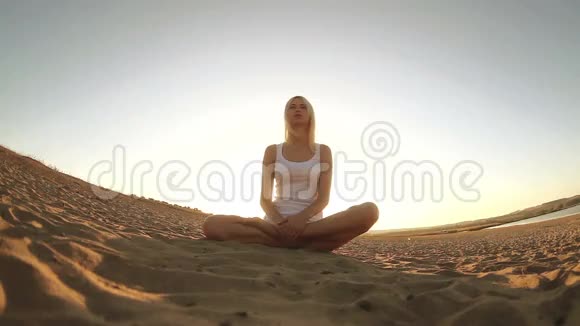 金发女人穿着白色衣服坐在沙滩上视频的预览图