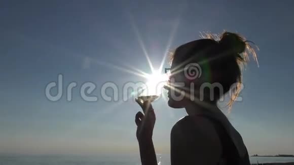 日落时分海滩上一个年轻迷人的女人在喝着玻璃视频的预览图