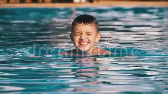 快乐的男孩在一个有蓝色水的游泳池里游泳慢动作视频的预览图