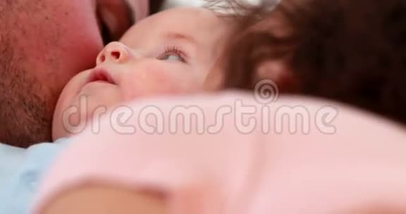 穿着蓝色婴儿服的男孩被快乐的父母在床上亲吻视频的预览图
