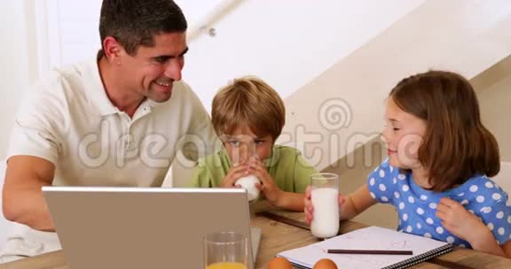 爸爸和孩子们一起在早餐桌上使用笔记本电脑视频的预览图