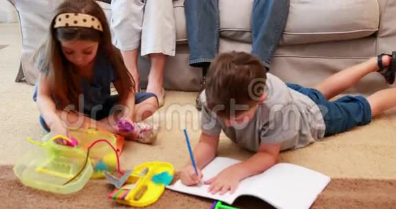 年轻的兄弟姐妹在地毯上做工艺品而父母则看着视频的预览图