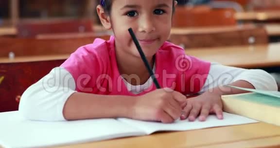 教室里可爱的小女孩在书上涂着颜色对着镜头微笑视频的预览图