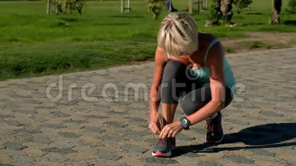 年长的女人把鞋带系在路上视频的预览图