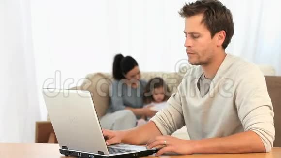 当妻子在给女儿读一本书时男人用笔记本电脑视频的预览图