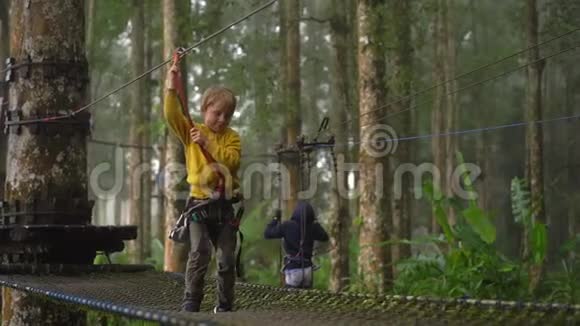 一个穿着安全装备的小男孩在森林探险公园的树梢上爬上了一条路线他是视频的预览图