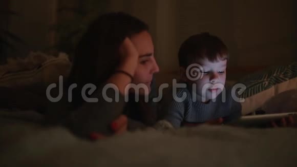 幸福的一家人母子躺在床上在他家的卧室里玩游戏屏幕上放着平板电脑视频的预览图