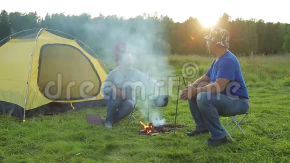 一个男人和一个女人在火炉边的帐篷附近用锅做饭视频的预览图