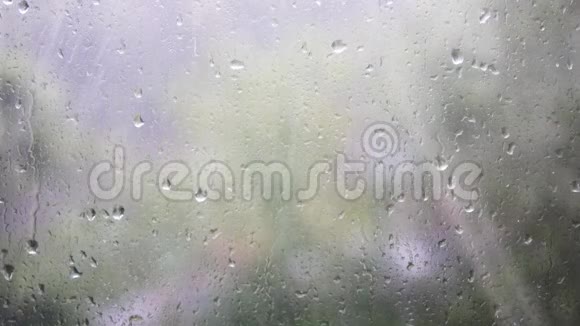 玻璃上水滴的特写雨滴在模糊背景的窗户玻璃上模糊的树和天空雨天视频的预览图