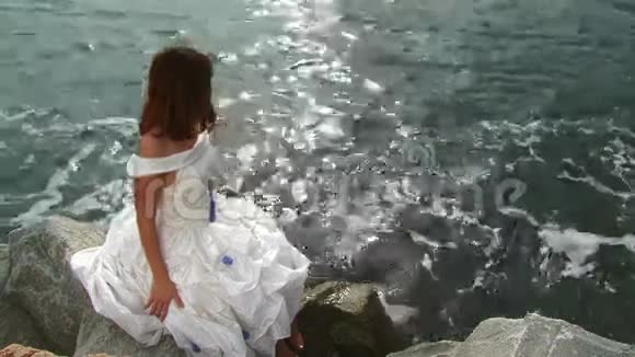 穿着白衣服坐在石头上的漂亮年轻女子视频的预览图