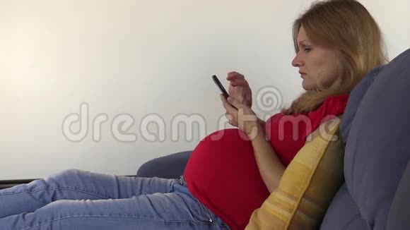 可爱的孕妇用智能手机浏览照片和上网视频的预览图