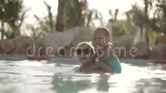 快乐漂亮的妈妈和女儿在游泳池里玩得开心视频的预览图