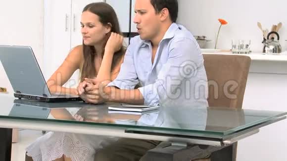 一对幸福的夫妇坐在桌旁看着笔记本电脑视频的预览图