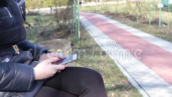 女孩打印一条信息在春天公园的智能手机上滚动页面视频的预览图